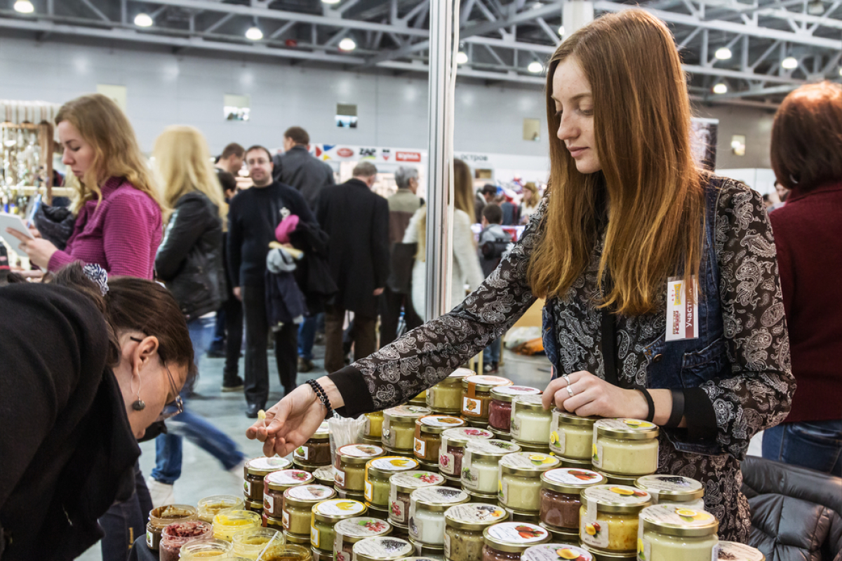 This is a photo of a salesman at a trade booth surrounded by jars of jams, jellies, and compotes.
