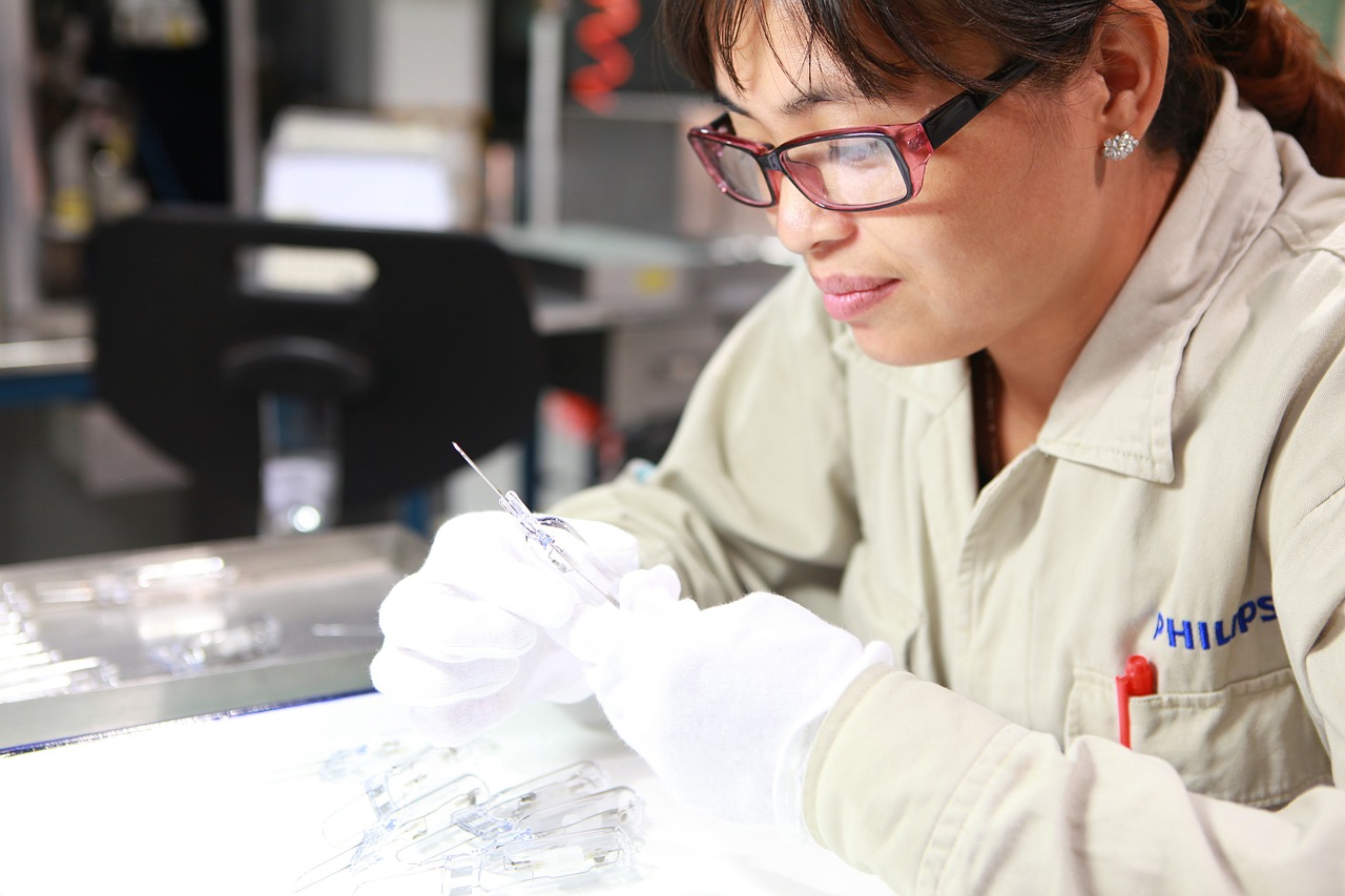This is an image of a female factory worker wearing a white lab coat and gloves.