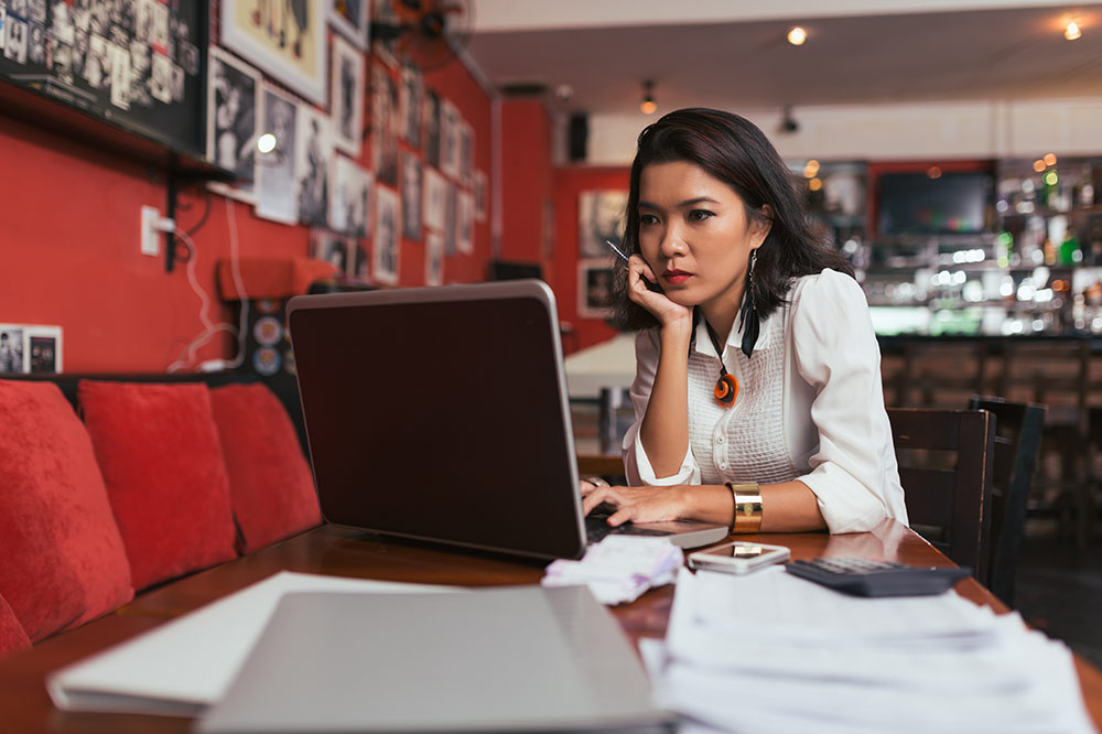 This is an image of a female business woman working on her laptop while sitting at a restaurant table.