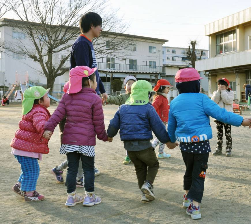 This is an image of a group of small children holding hands while playing a game while an adult male daycare worker looks on.