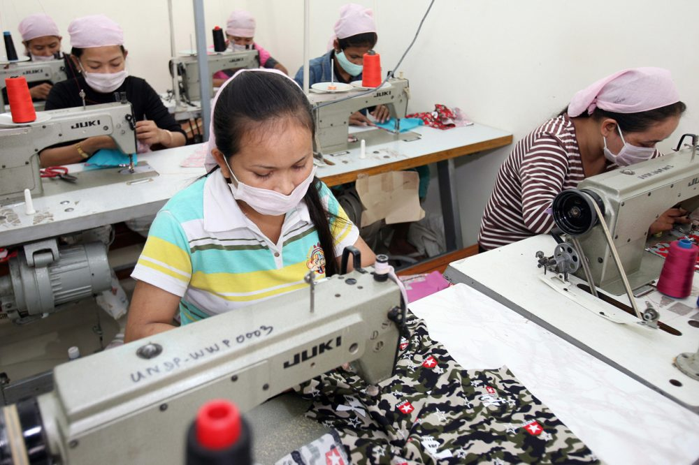 This is an image of six female factory workers wearing white masks as they sew clothes at machines.