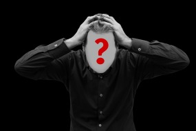 This is a photograph of a male with his hands on his head.  His face is covered by a big red question mark.