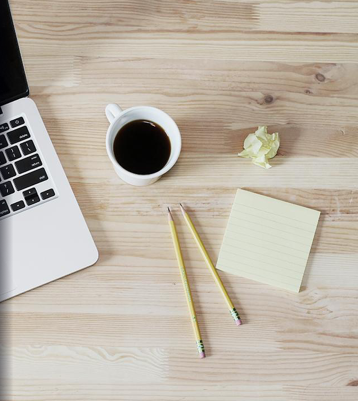 Image of a desk with a laptop, a coffee, and some papers.