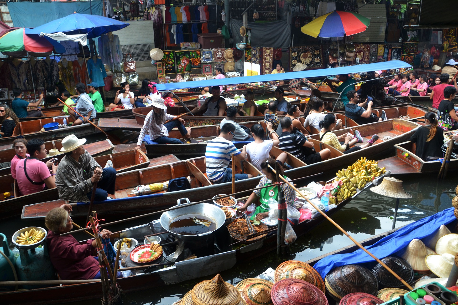 This is a photograph of a number of canoe style boats floating alongside each other, some with tourists, others with goods for sale or people cooking in them.