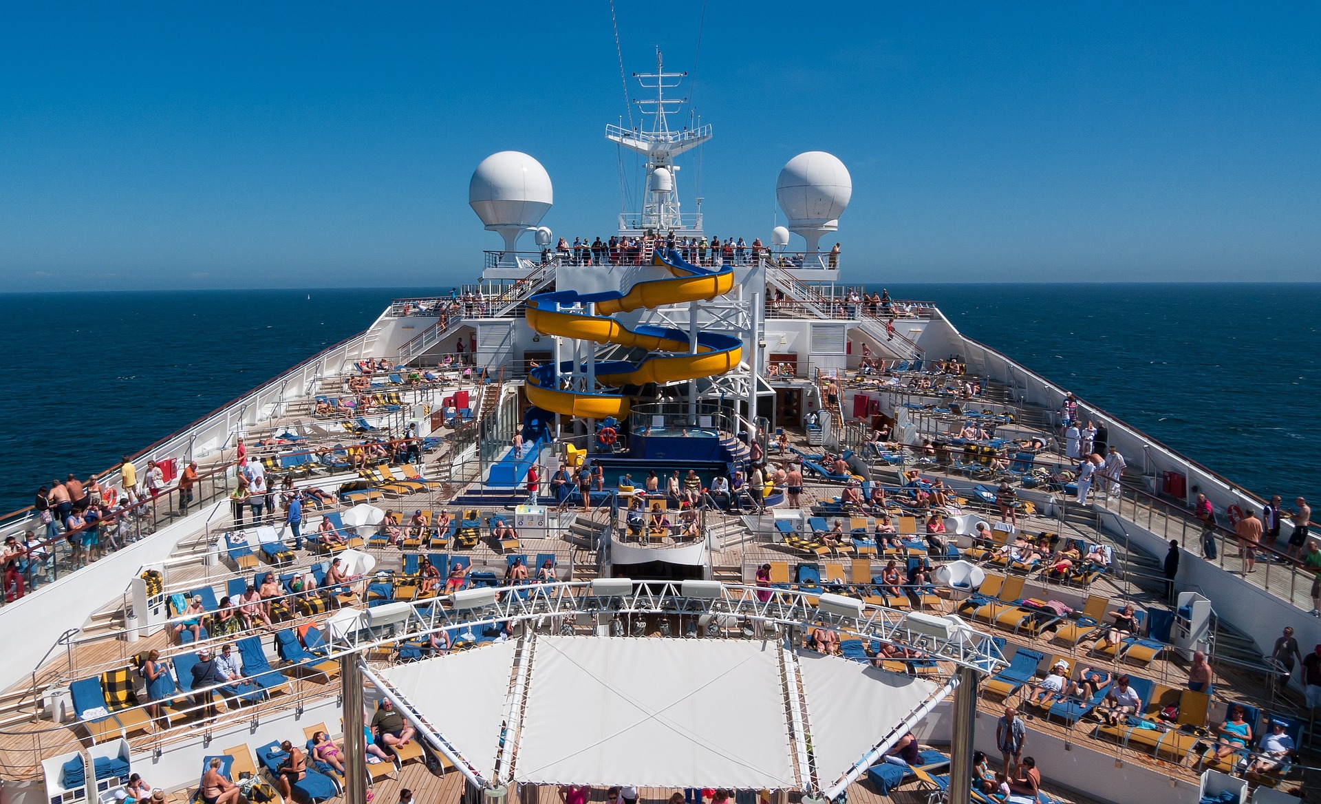 This is a photograph of the top deck of a cruise ship. It shows a waterslide and many lounge chairs.
