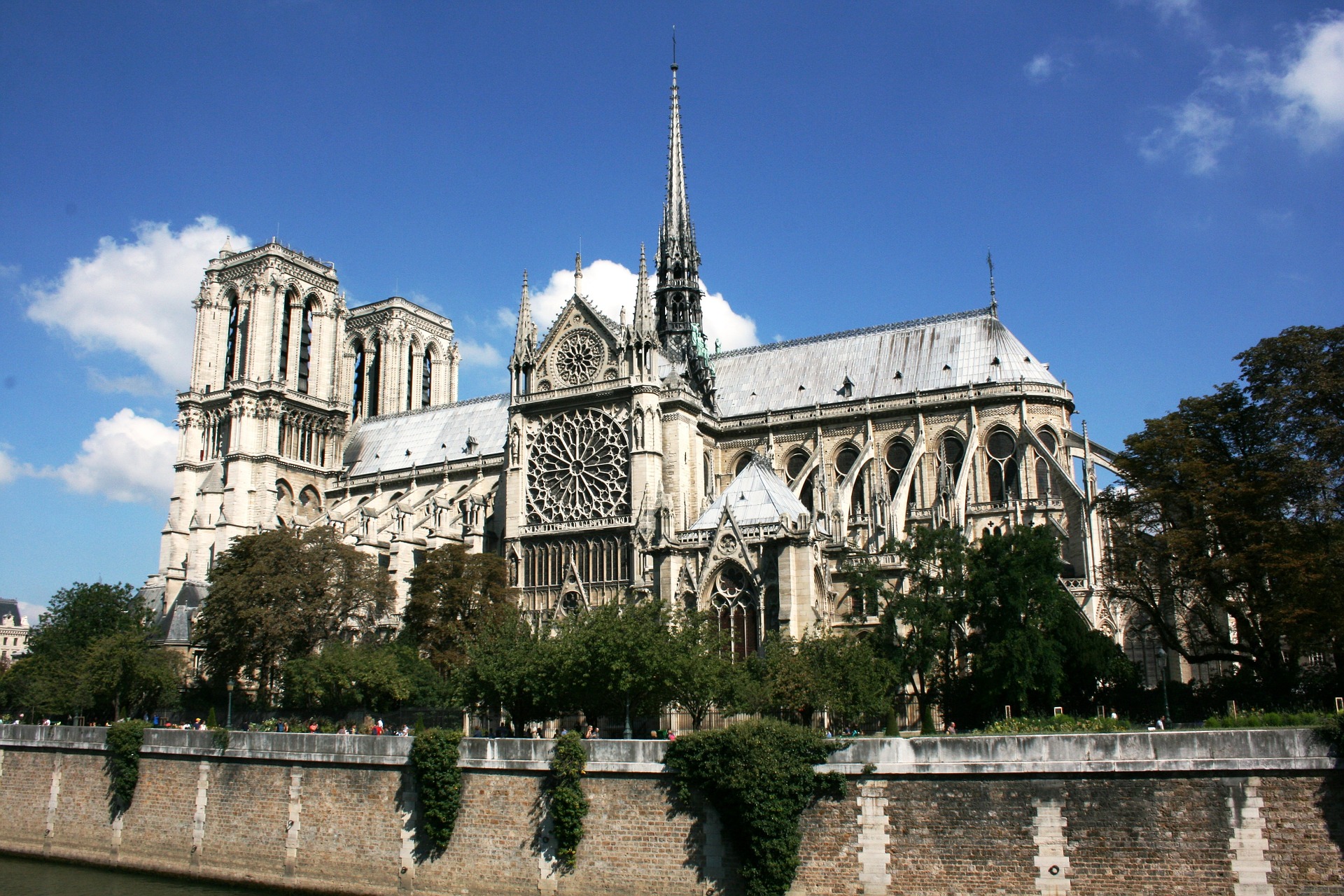 This is a photograph of a large cathedral made of white stone. A spire, rose window and flying buttresses are visible. 