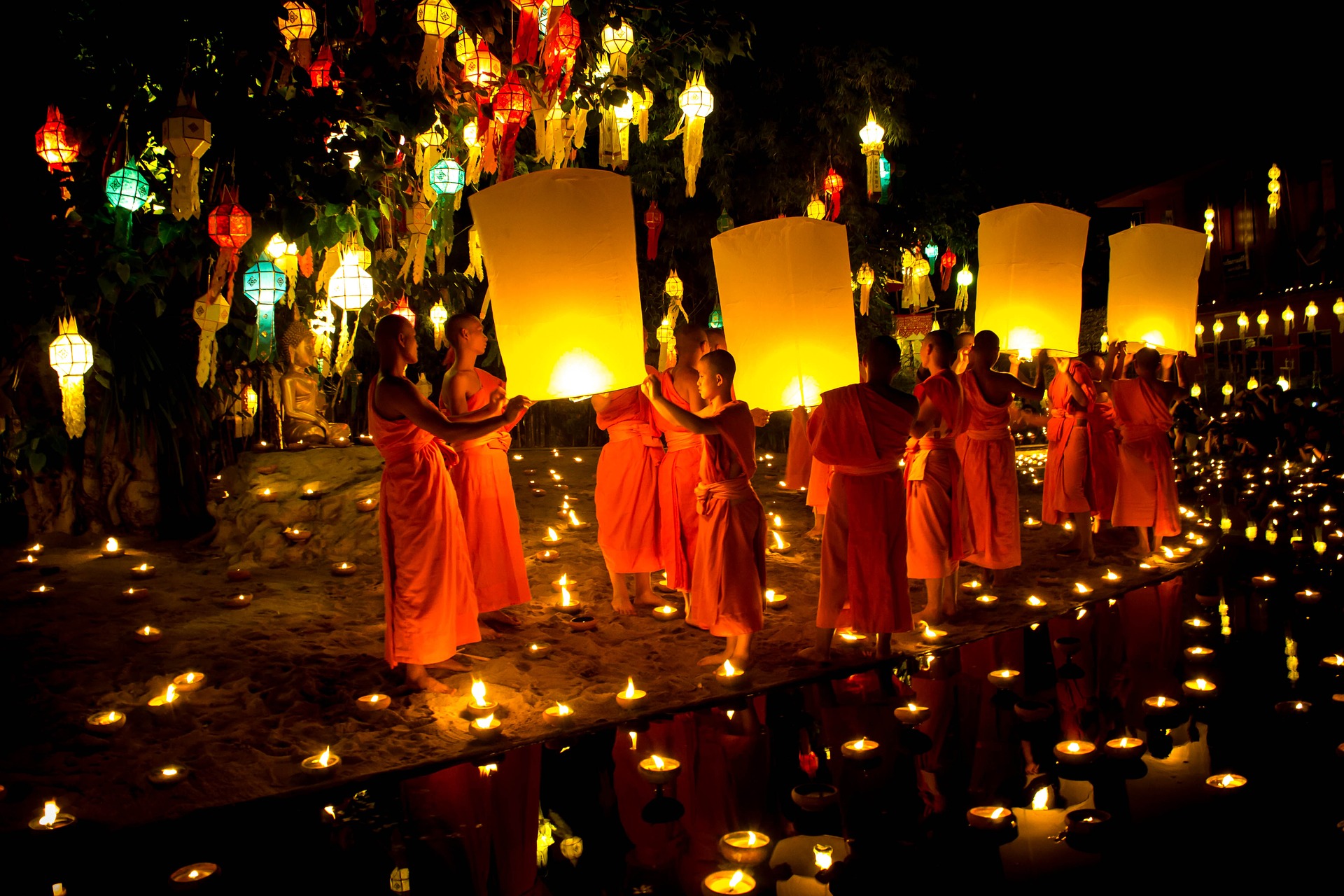 This is a photograph of a group of Buddhist monks wearing orange robes and holding lit paper lanterns at night.