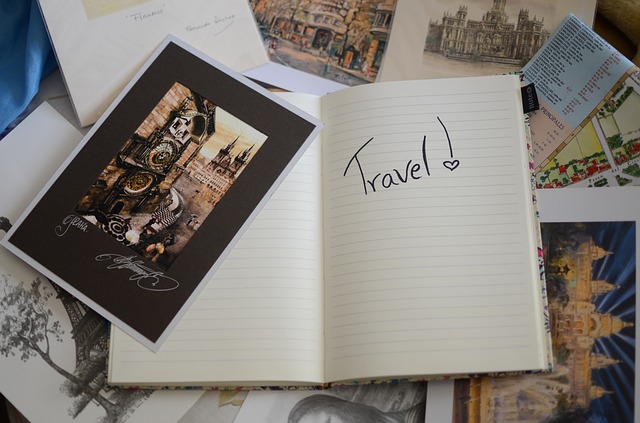 This is a photograph of a notebook with the work Travel written across it and a postcard beside it.