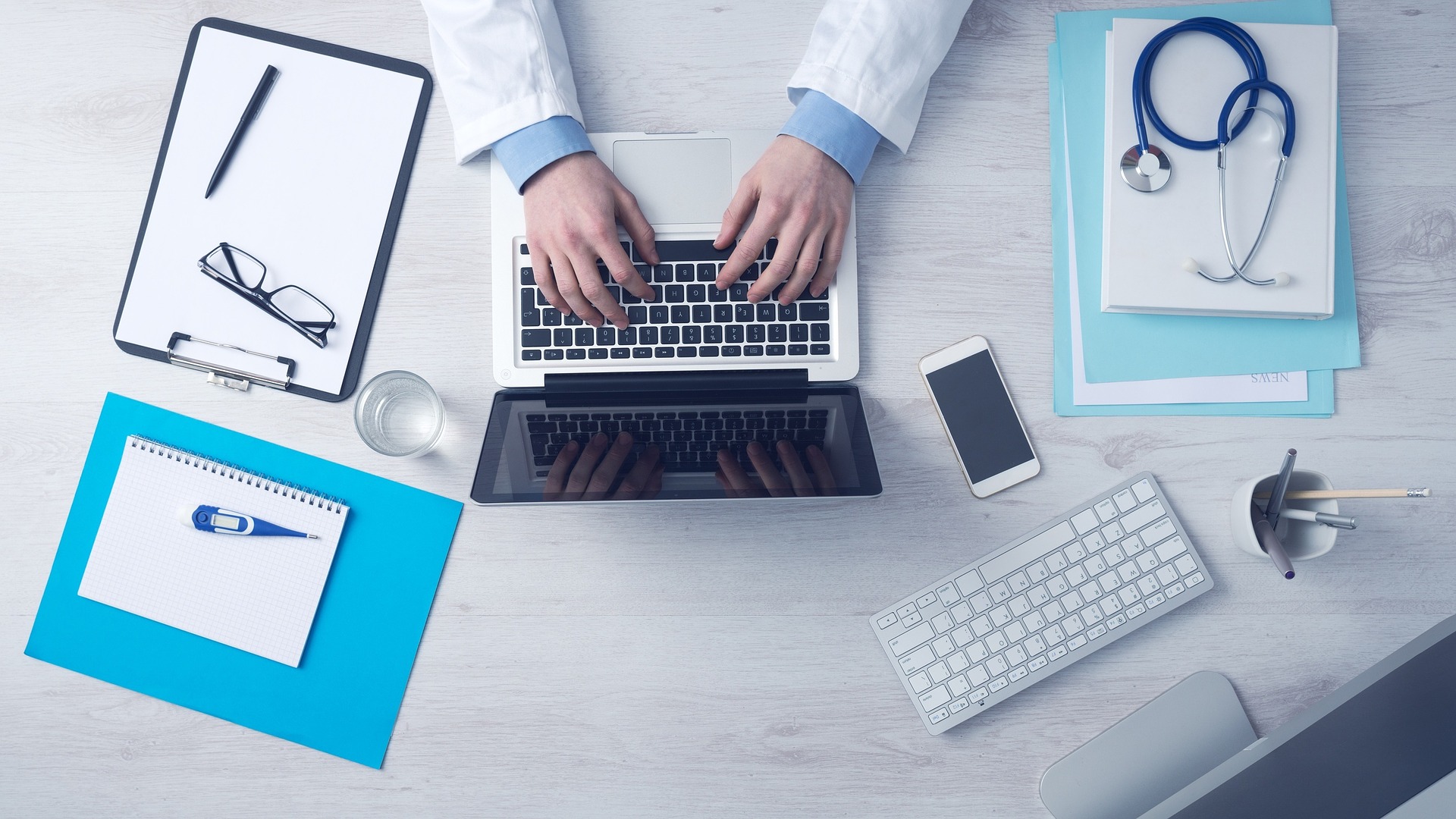 This is a photograph of a doctor’s desk with a laptop, clipboard, and stethoscope.
