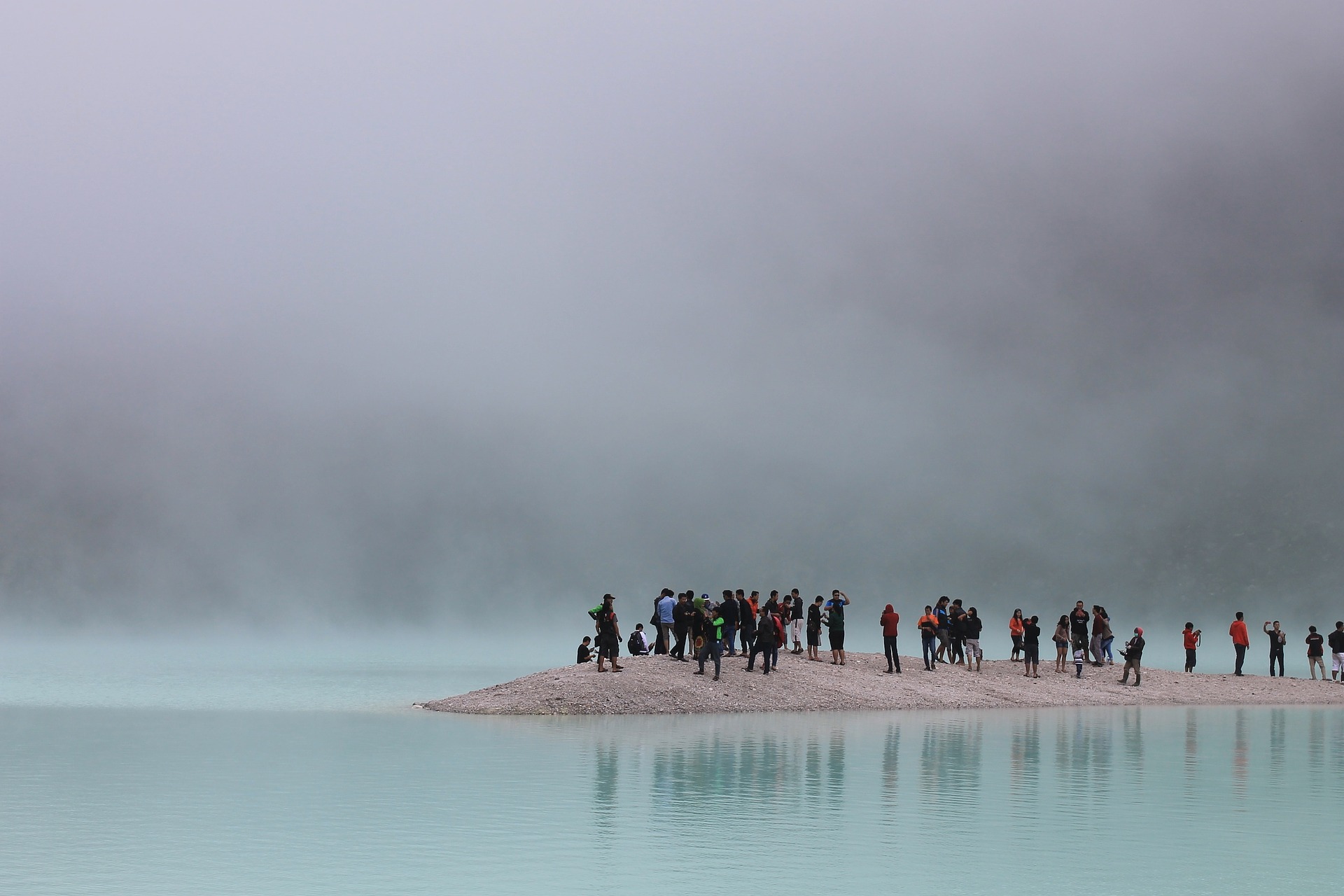 This is a photograph of a large group of tourists standing on a low piece of land surrounded by water. 