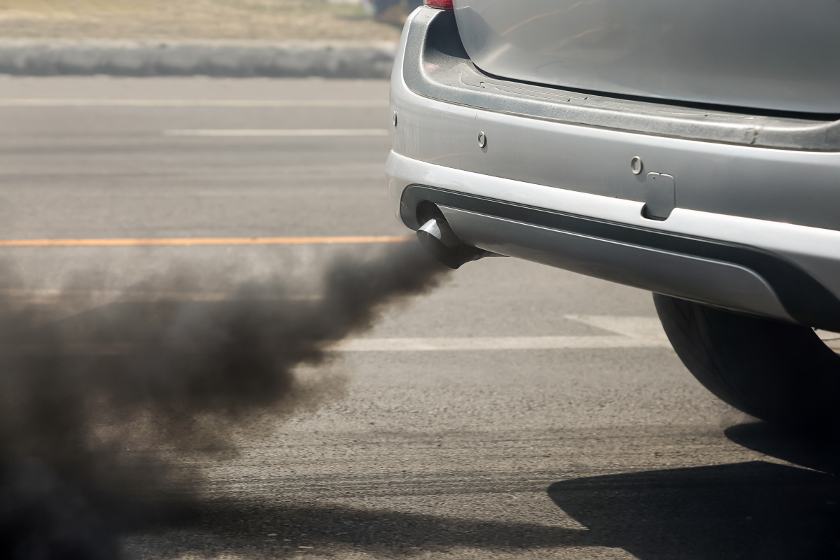 This is a photograph of the back bumper of a car with thick black exhaust coming out of the tailpipe. 