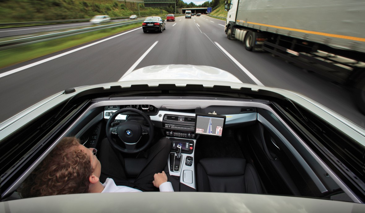 This is an image taken from above a convertible car looking inside, as it travels down a three-lane highway. The driver is not touching the steering wheel.