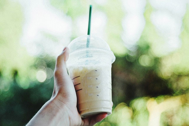 A hand holding a single-use cup with a plastic straw