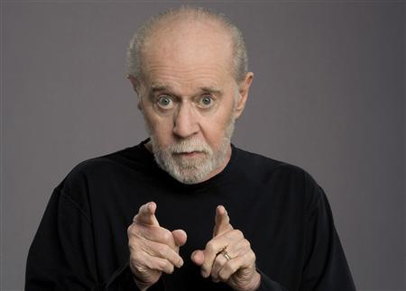 The comedian George Carlin is pictured pointing two fingers at the viewer.