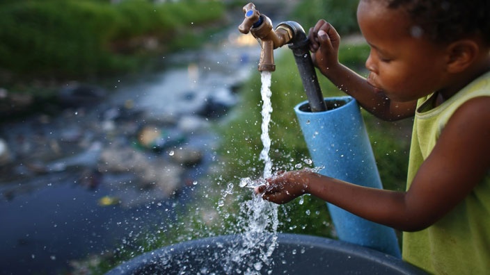 This photograph shows a child holding her hand under an open tap.