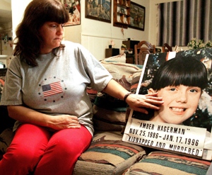 This is a photograph of an middle-aged woman sitting on a couch touching a poster with a photograph of a young girl with the words: Amber Hagerman - November 26, 1986 to January 17, 1996, kidnapped and murdered. 