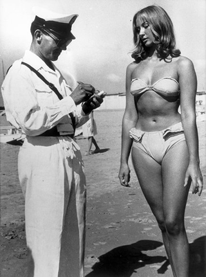 This is an image of a woman wearing a bikini. She is getting a ticket from a police officer because she is wearing clothing that is immodest.
