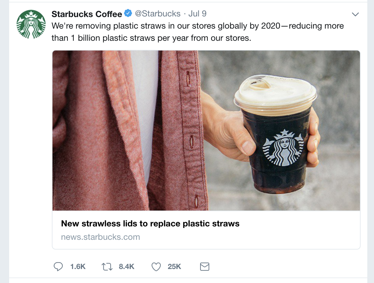 This is a close up of a person's mid section and their left hand, holding a clear Starbucks plastic cup that is filled with dark coffee and features a new strawless lid. The Starbucks Coffee tweet above this image states: We're removing plastic straws in our stores globally by 2020 reducing more than 1 billion plastic straws per year from our stores.