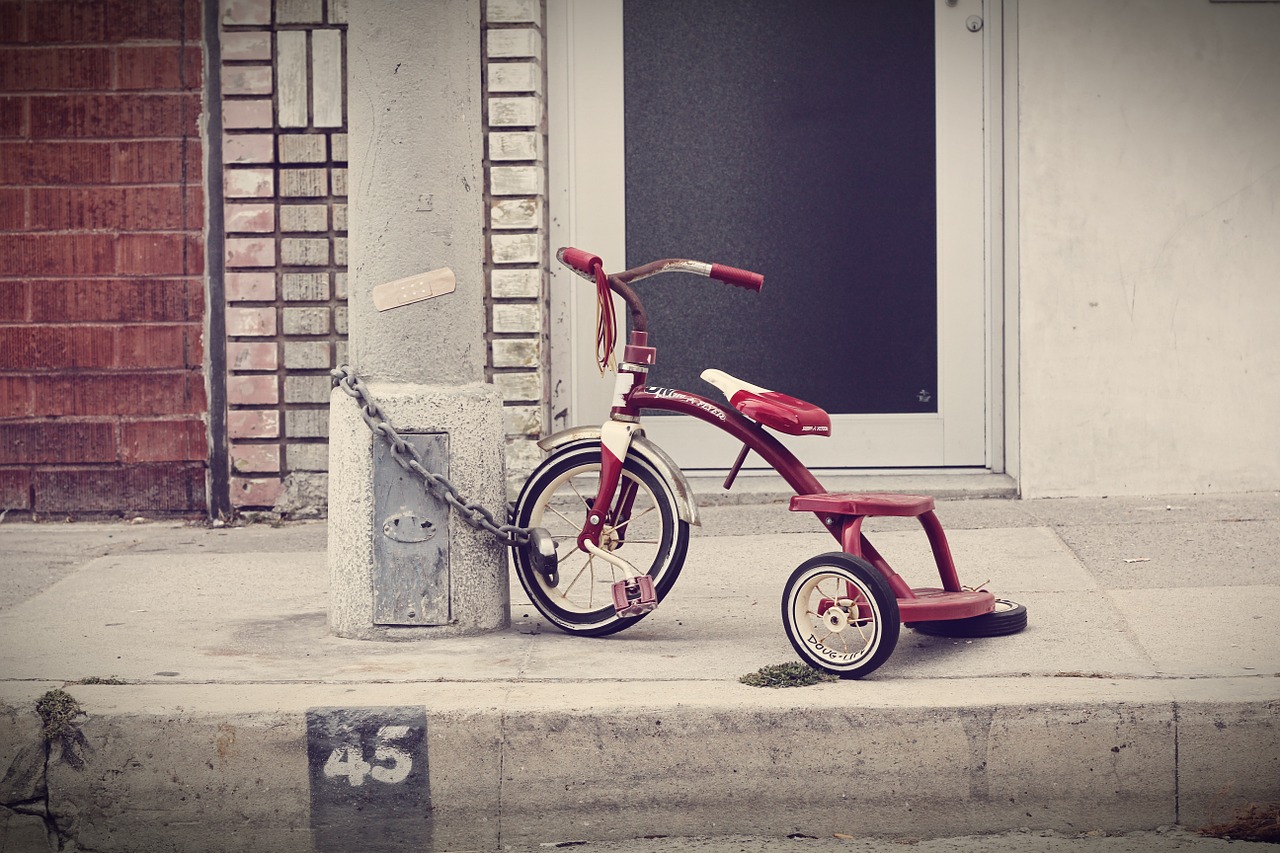 This is an image of a red tricycle that is locked to a cement block using a thick chain.