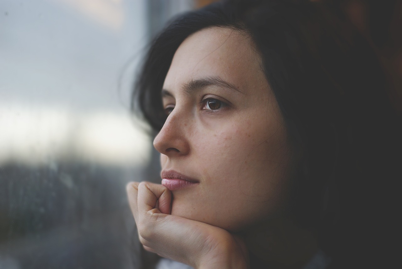 This is a close up image of a woman who is holding her chin while staring out a window.