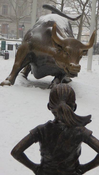 This is an image of two bronze statues, one of a charging bull, and the other, of a little girl standing up to it.