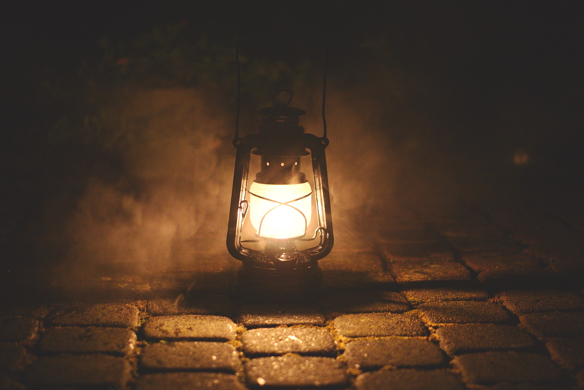 This is an image of a lit kerosene lamp resting on stone tiles, illuminating the fog all around it.