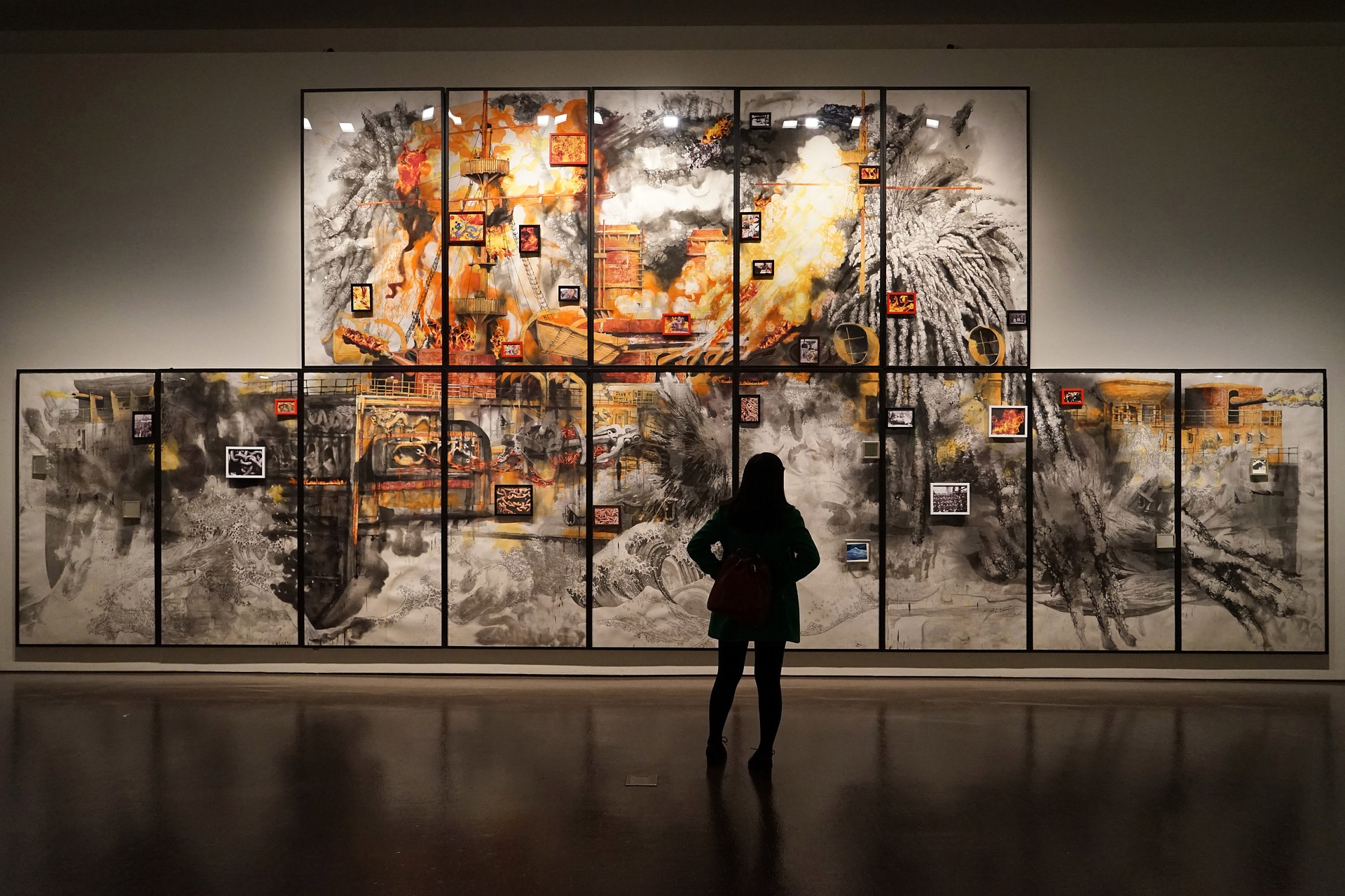 This is an image of the silhouette of a person looking at a series of paintings on a gallery wall, that, when combined, create a larger single image.