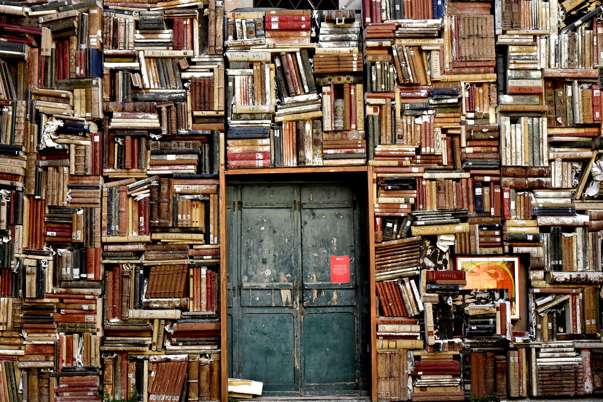 This is an image of a wall of books with a metal door in the middle.