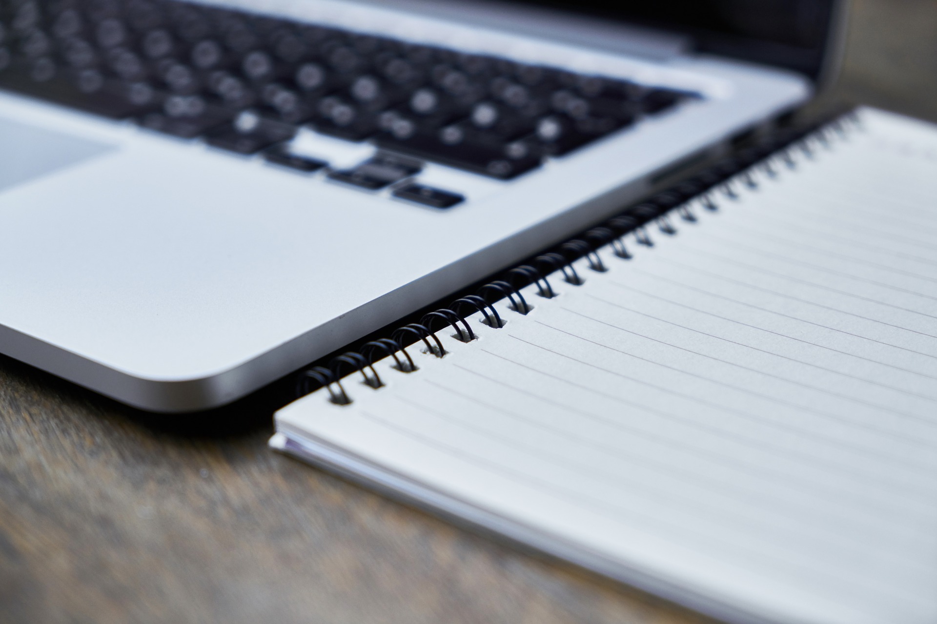 This is an image of a close up of a laptop and a spiral bound notebook side by side.