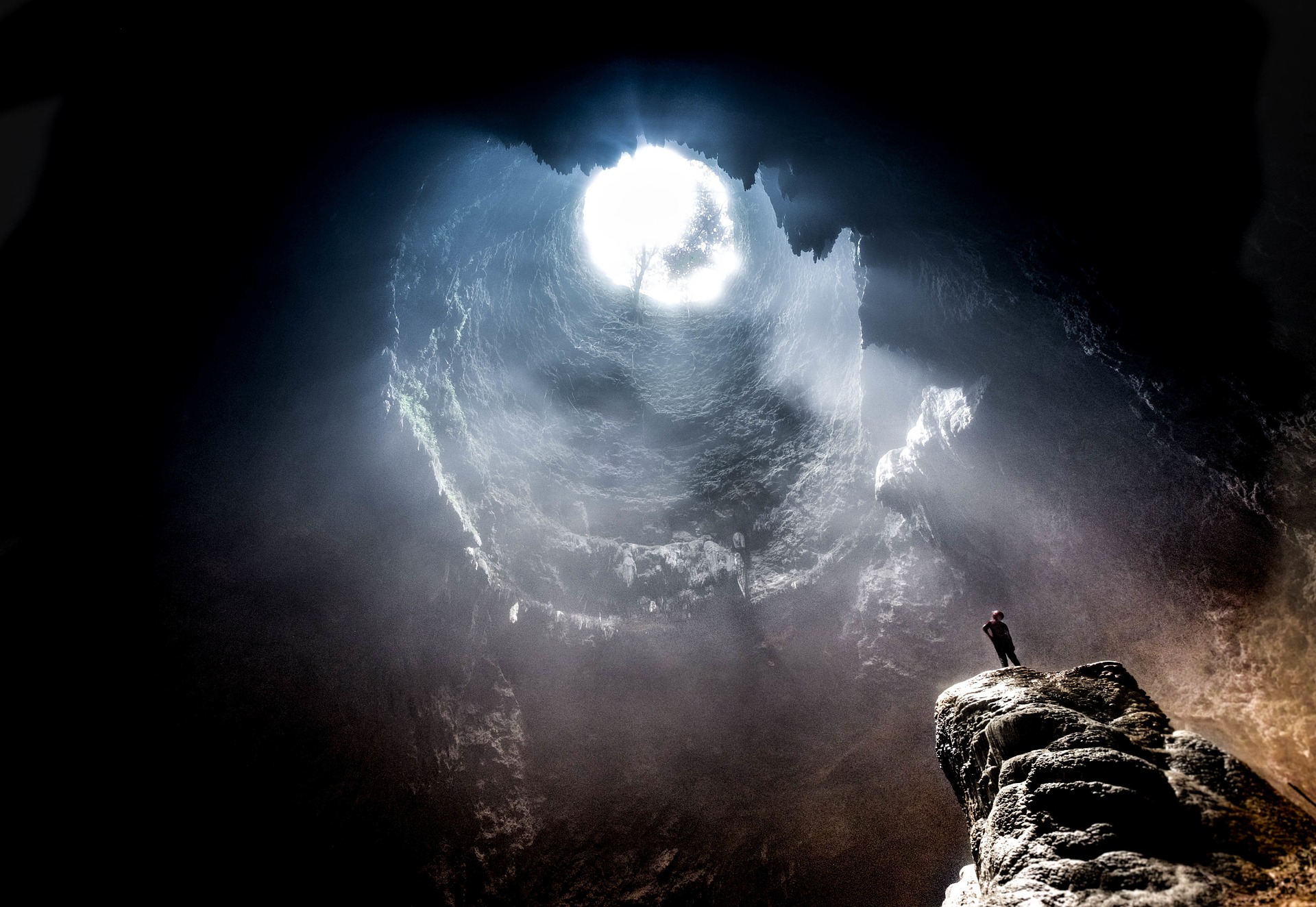 This is an image of a person at the bottom of a cave looking up into the light that is coming through an opening.