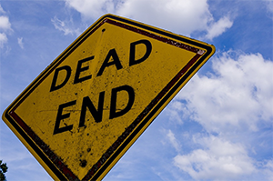 This is an image of a yellow and black sign that reads “Dead End” with a blue sky and clouds in the background.
