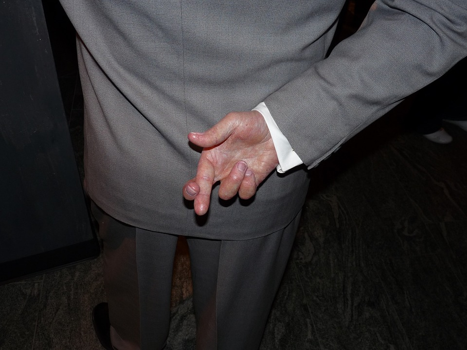 This is an image of a man with his back to the viewer; his right hand is behind his back and his fingers are crossed.
