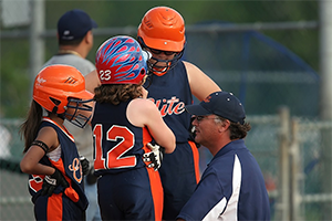 This is an image of three young female softball players getting advice from their coach.