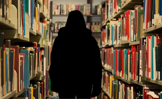 This is an image of a silhouette of a person walking down an aisle and surrounded by filled bookshelves.