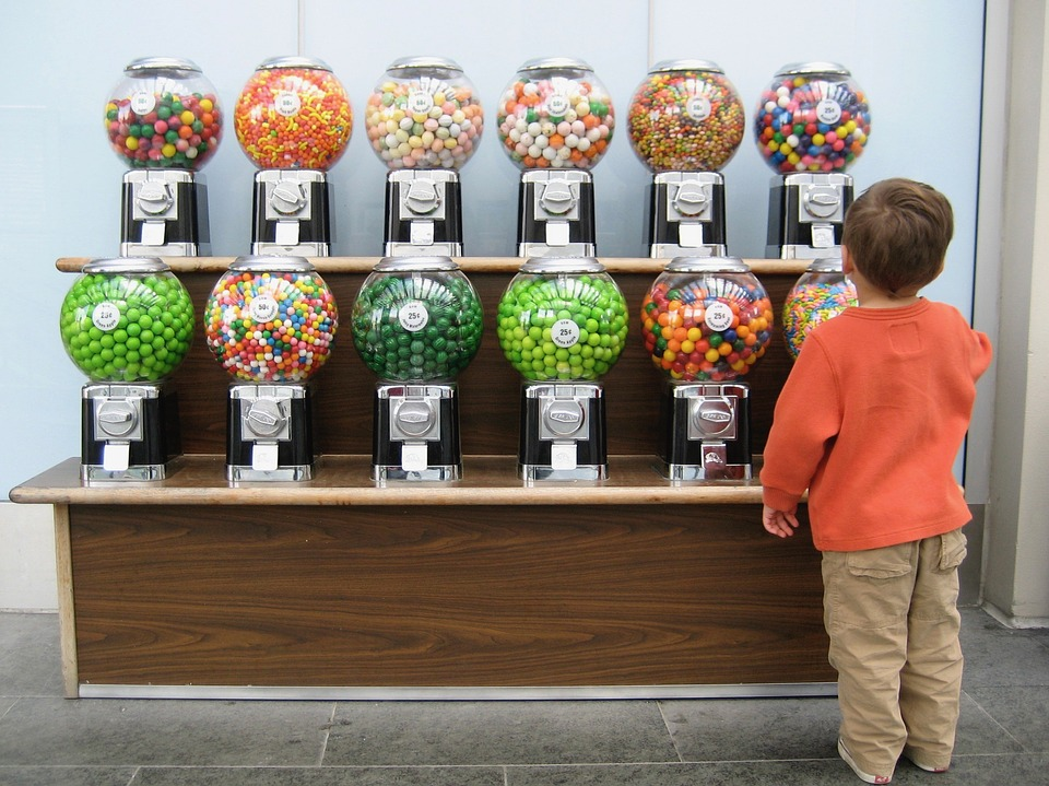 This is an image of a male child facing two rows of twelve candy dispensers, each with different options.