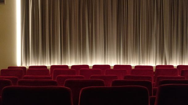 This is an image of a stage with closed curtains and rows of empty red cushioned seats.