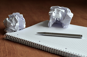 This is an image of a blank pad of paper with a pen on it and two crumbled up paper balls off to the side.