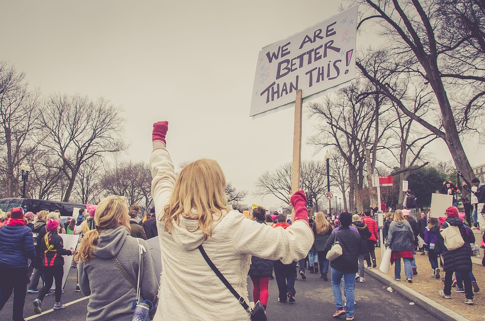 This is an image of a group of people protesting; a woman holds up a sign that reads, &lsquo;We are better than this!&rsquo;