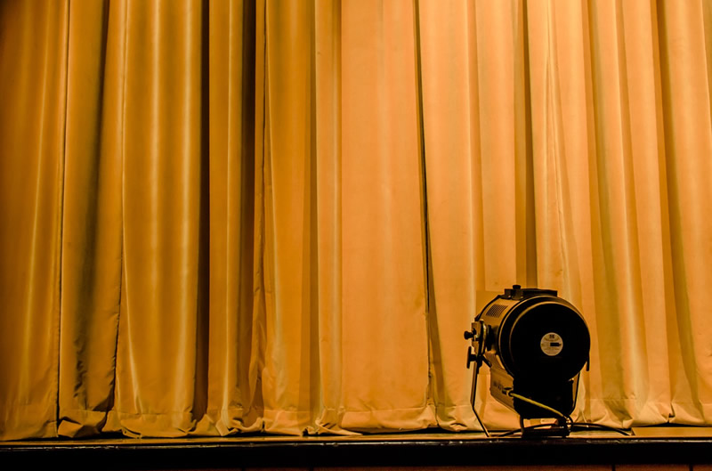 This is an image of a closed yellow curtain with a spotlight sitting on the stage.