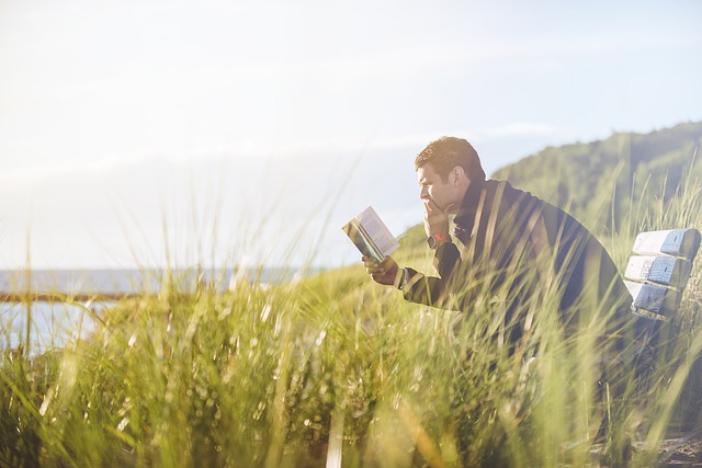 Un jeune homme lit un livre sur un banc au bord de l'eau.