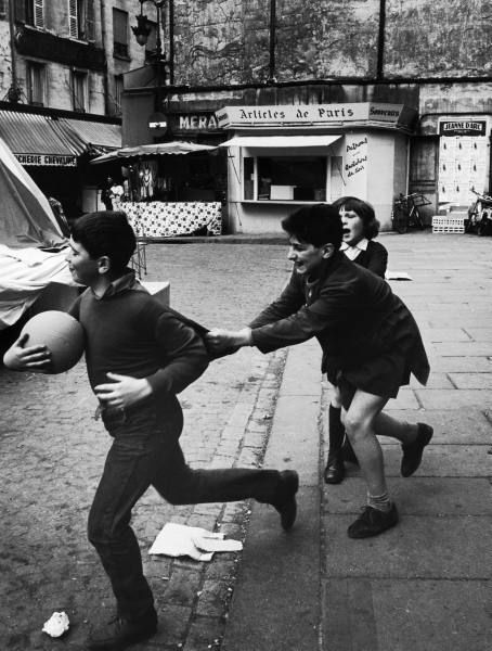 Trois enfants s'amusent avec un ballon dans une rue de Paris.