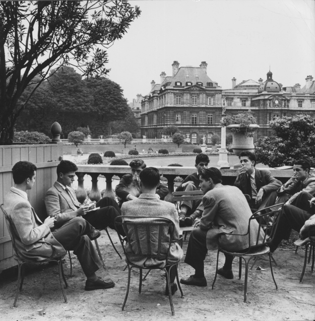 Quelques jeunes hommes sont en conversation autour d'une table pres d'une fontaine a Paris.