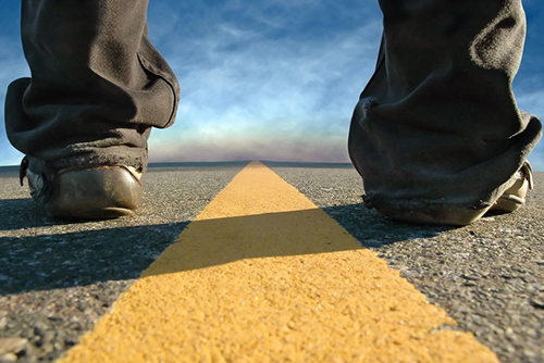 This is an image of a pair of feet standing on a road on either side of a median line extending to the horizon.