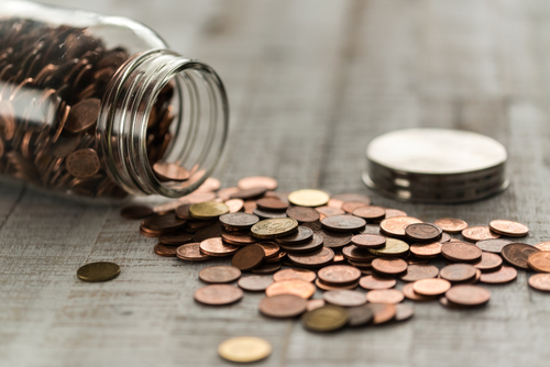 This is an image of an overturned jar of pennies with the coins spilling out.