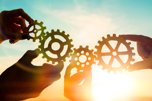 This is an image of a hands holding a set of interlocking gears against a setting sun.