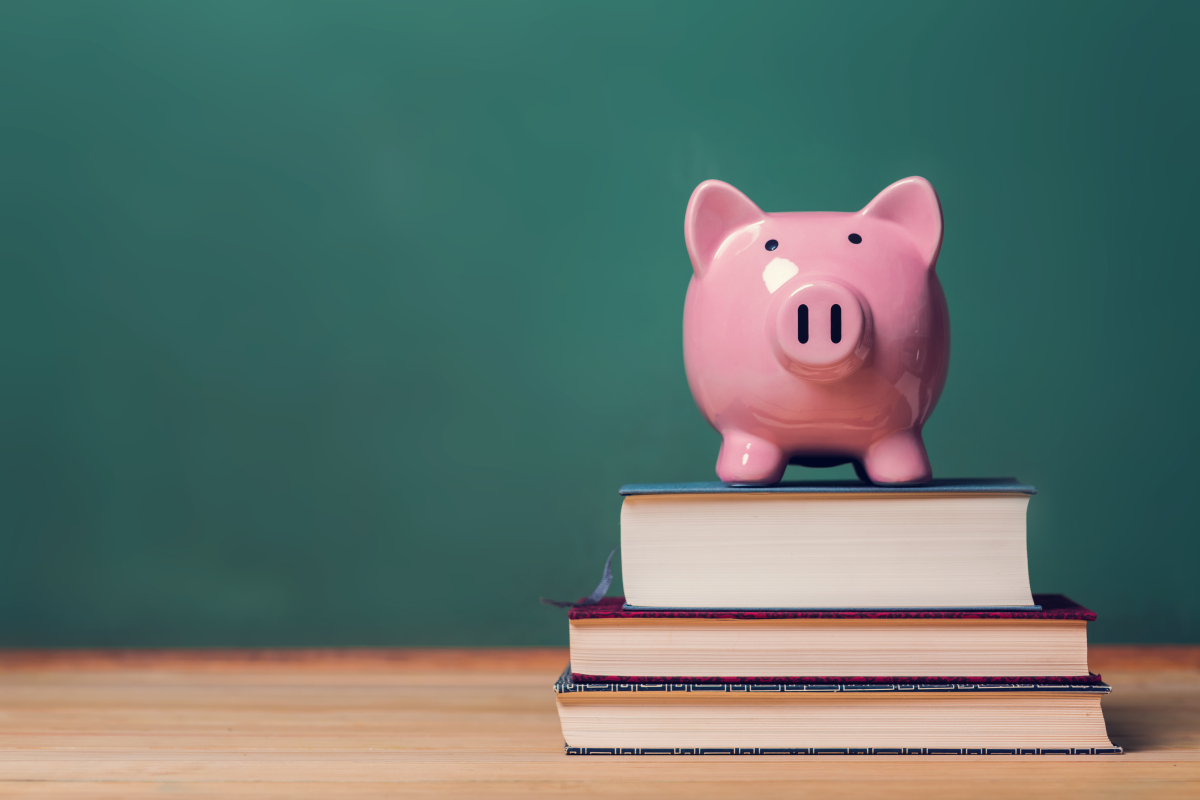 This graphic shows a pink piggy bank sitting on top of books with a chalkboard in the background.