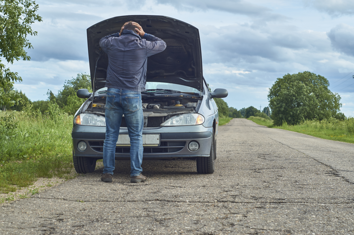This graphic shows a worried man holding his head standing near a broken down car with its hood raised on the road.