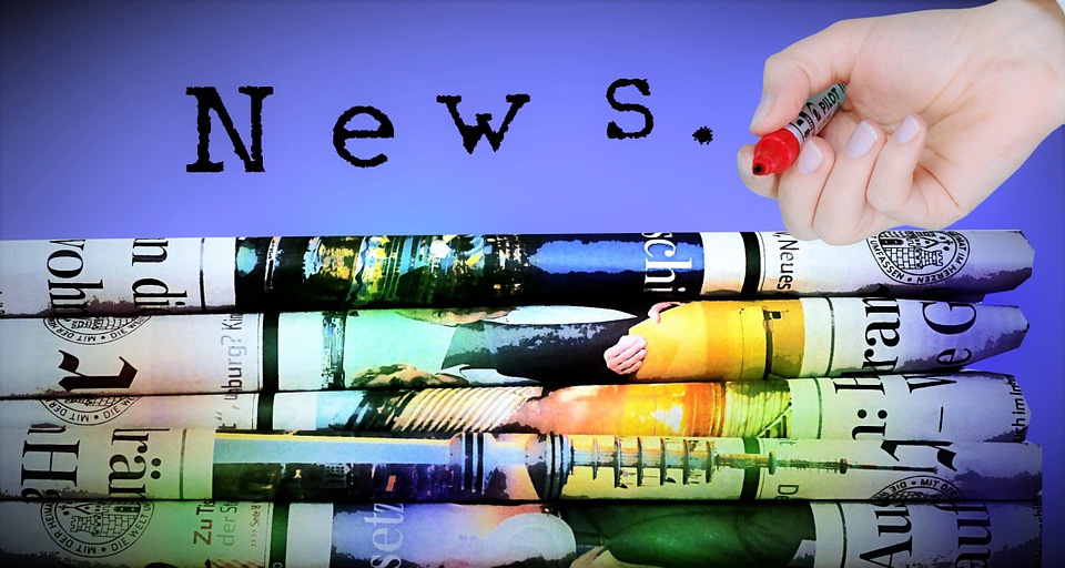 This is an image of a stack of newspapers with a person’s hand holding a highlighter resting on the top.
