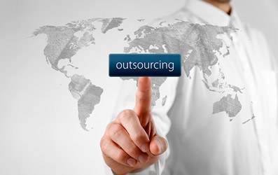 This is an image of a man using his finger to press a button that says &lsquo;outsourcing&rsquo;. The button is on a glass screen etched with a simple map of the world.
