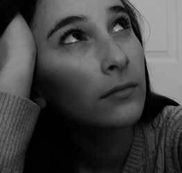 This is a a headshot of a young woman with her hand on the side of her head, staring upwards, with a pondering look on her face.
